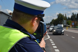 Policjant ruchu drogowego z ręcznym miernikiem prędkości. W tle przejeżdżające pojazdy.