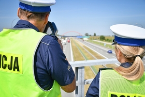 Policjant i policjantka ruchu drogowego podczas działań stoją na przejeździe nad autostradą. W tle widać jadące pojazdy