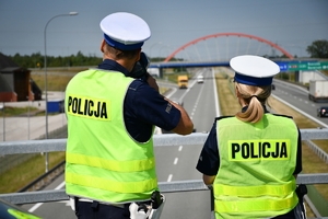 Policjant i policjantka ruchu drogowego podczas działań stoją na przejeździe nad autostradą. W tle widać jadące pojazdy