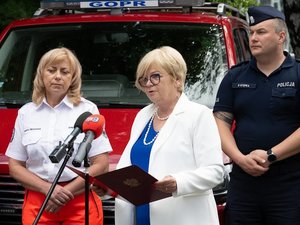 Wojewoda Podkarpacki, przedstawiciele służb, inspekcji i straży ustawieni na tle pojazdów służbowych podczas briefingu udzielają informacji mediom.