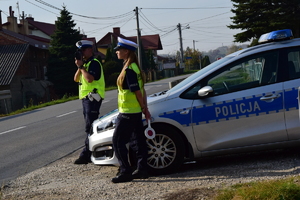 Dwoje policjantów stojących przy radiowozie obok ulicy