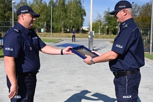 Policjanci i zaproszeni goście podczas uroczystości otwarcia komisariatu. Policjanci stoją na parkingu przed budynkiem.