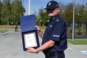 Policjanci i zaproszeni goście podczas uroczystości otwarcia komisariatu. Policjanci stoją na parkingu przed budynkiem.