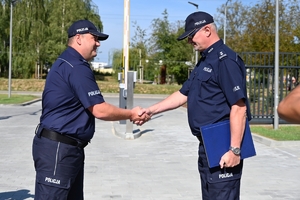 Policjanci i zaproszeni goście podczas uroczystości otwarcia komisariatu. Policjanci stoją na parkingu przed budynkiem.