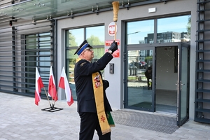 Policjanci i zaproszeni goście podczas uroczystości otwarcia komisariatu. Policjanci stoją na parkingu przed budynkiem.