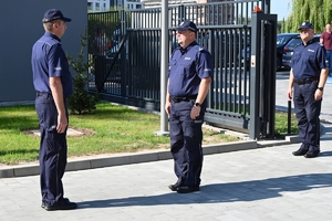 Policjanci i zaproszeni goście podczas uroczystości otwarcia komisariatu. Policjanci stoją na parkingu przed budynkiem.