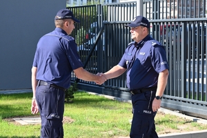 Policjanci i zaproszeni goście podczas uroczystości otwarcia komisariatu. Policjanci stoją na parkingu przed budynkiem.