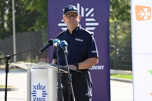 Policjanci i zaproszeni goście podczas uroczystości otwarcia komisariatu. Policjanci stoją na parkingu przed budynkiem.