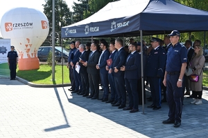 Policjanci i zaproszeni goście podczas uroczystości otwarcia komisariatu. Policjanci stoją na parkingu przed budynkiem.