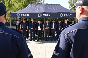 Policjanci i zaproszeni goście podczas uroczystości otwarcia komisariatu. Policjanci stoją na parkingu przed budynkiem.