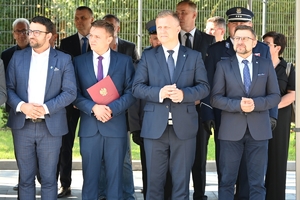 Policjanci i zaproszeni goście podczas uroczystości otwarcia komisariatu. Policjanci stoją na parkingu przed budynkiem.