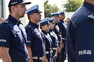 Policjanci i zaproszeni goście podczas uroczystości otwarcia komisariatu. Policjanci stoją na parkingu przed budynkiem.