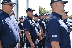 Policjanci i zaproszeni goście podczas uroczystości otwarcia komisariatu. Policjanci stoją na parkingu przed budynkiem.