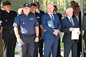 Policjanci i zaproszeni goście podczas uroczystości otwarcia komisariatu. Policjanci stoją na parkingu przed budynkiem.