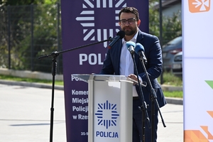 Policjanci i zaproszeni goście podczas uroczystości otwarcia komisariatu. Policjanci stoją na parkingu przed budynkiem.