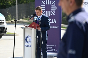 Policjanci i zaproszeni goście podczas uroczystości otwarcia komisariatu. Policjanci stoją na parkingu przed budynkiem.