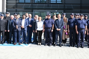 Policjanci i zaproszeni goście podczas uroczystości otwarcia komisariatu. Policjanci stoją na parkingu przed budynkiem.