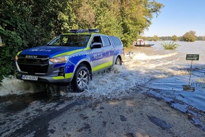 Policjanci podczas działań na terenach popowodziowych. Funkcjonariusze w specjalnych strojach patrolują tereny zalane przez wodę