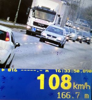 Zdjęcie z policyjnego wideorejestratora. Widoczny samochód, w tle pojazdy. Poniżej napis 108 km/h