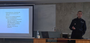 Funkcjonariusz razem ze studentami ELSA podczas prowadzenia zajęć - policjant po prawej, po lewej fragment ekranu rzutnika z prezentacją.
