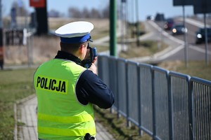 Umundurowany policjant wykonujący pomiar prędkości pojazdom poruszającym się po drodze.