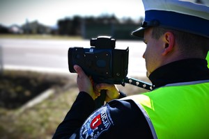 Policjant wykonujący pomiar prędkości pojazdów poruszających się po drodze.