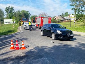 Zdjęcie z miejsca zdarzenia, na którym widoczne są wozy strażackie, policjant i uszkodzone pojazdy.