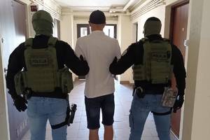 Policjanci (po lewej i po prawej) prowadzą zatrzymanego (w środku).