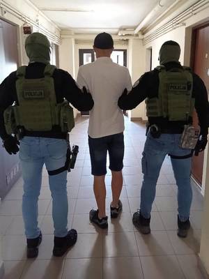 Policjanci (po lewej i po prawej) prowadzą zatrzymanego (w środku).