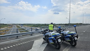 Policjant ruchu drogowego stojący na wiadukcie i sprawdzający odległość między pojazdami, na pierwszym planie dwa motocykle służbowe