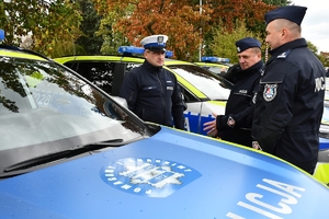 Policjanci i nowe radiowozy na placu.