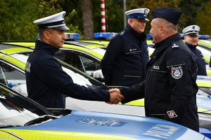 Policjanci i nowe radiowozy na placu.
