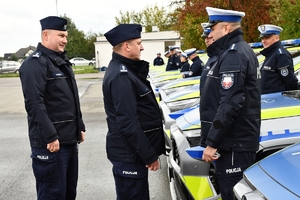 Policjanci i nowe radiowozy na placu.