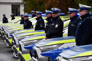 Policjanci i nowe radiowozy na placu.
