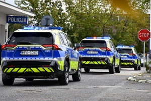 Policjanci i nowe radiowozy na placu.
