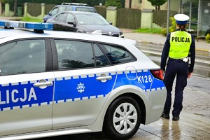 Zdjęcie radiowozu obok, którego stoi umundurowana policjantka.