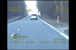 Widoczny samochód jadący przed radiowozem. W dolnym lewym rogu pojawia się żółty napis 157.4 km/h