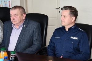 Uczestnicy spotkania w sali sztabowej Komendy Wojewódzkiej Policji w Rzeszowie. Uczestnicy siedzą przy stole, w tle na ścianie logo Komendy Wojewódzkiej Policji w Rzeszowie i napis  Komenda Wojewódzka Policji w Rzeszowie.