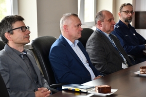 Uczestnicy spotkania w sali sztabowej Komendy Wojewódzkiej Policji w Rzeszowie. Uczestnicy siedzą przy stole, w tle na ścianie logo Komendy Wojewódzkiej Policji w Rzeszowie i napis  Komenda Wojewódzka Policji w Rzeszowie.