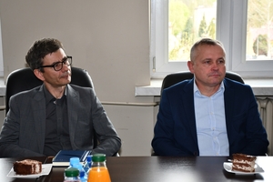 Uczestnicy spotkania w sali sztabowej Komendy Wojewódzkiej Policji w Rzeszowie. Uczestnicy siedzą przy stole, w tle na ścianie logo Komendy Wojewódzkiej Policji w Rzeszowie i napis  Komenda Wojewódzka Policji w Rzeszowie.