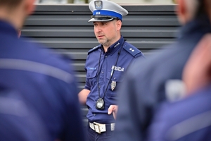 Policjanci na placu manewrowym - podczas konkurencji jazdy motocyklem. Policjant w kasku i na motocyklu jedzie po torze.