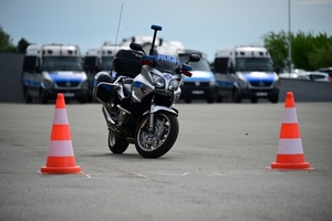 Policjanci na placu manewrowym - podczas konkurencji jazdy motocyklem. Policjant w kasku i na motocyklu jedzie po torze.