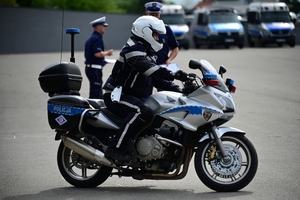 Policjanci na placu manewrowym - podczas konkurencji jazdy motocyklem. Policjant w kasku i na motocyklu jedzie po torze.