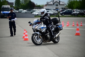 Policjanci na placu manewrowym - podczas konkurencji jazdy motocyklem. Policjant w kasku i na motocyklu jedzie po torze.