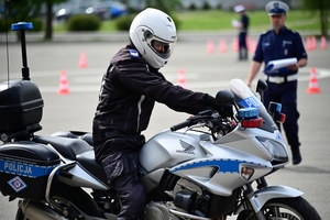 Policjanci na placu manewrowym - podczas konkurencji jazdy motocyklem. Policjant w kasku i na motocyklu jedzie po torze.