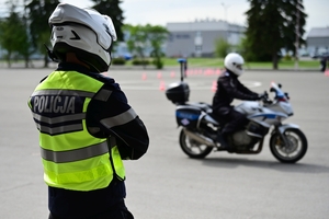 Policjanci na placu manewrowym - podczas konkurencji jazdy motocyklem. Policjant w kasku i na motocyklu jedzie po torze.