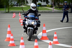 Policjanci na placu manewrowym - podczas konkurencji jazdy motocyklem. Policjant w kasku i na motocyklu jedzie po torze.