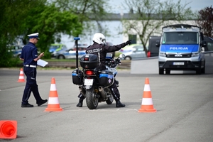 Policjanci na placu manewrowym - podczas konkurencji jazdy motocyklem. Policjant w kasku i na motocyklu jedzie po torze.