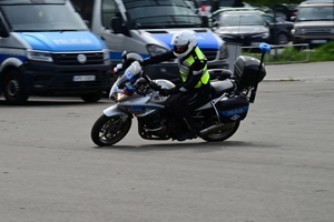 Policjanci na placu manewrowym - podczas konkurencji jazdy motocyklem. Policjant w kasku i na motocyklu jedzie po torze.