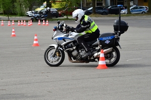 Policjanci na placu manewrowym - podczas konkurencji jazdy motocyklem. Policjant w kasku i na motocyklu jedzie po torze.
